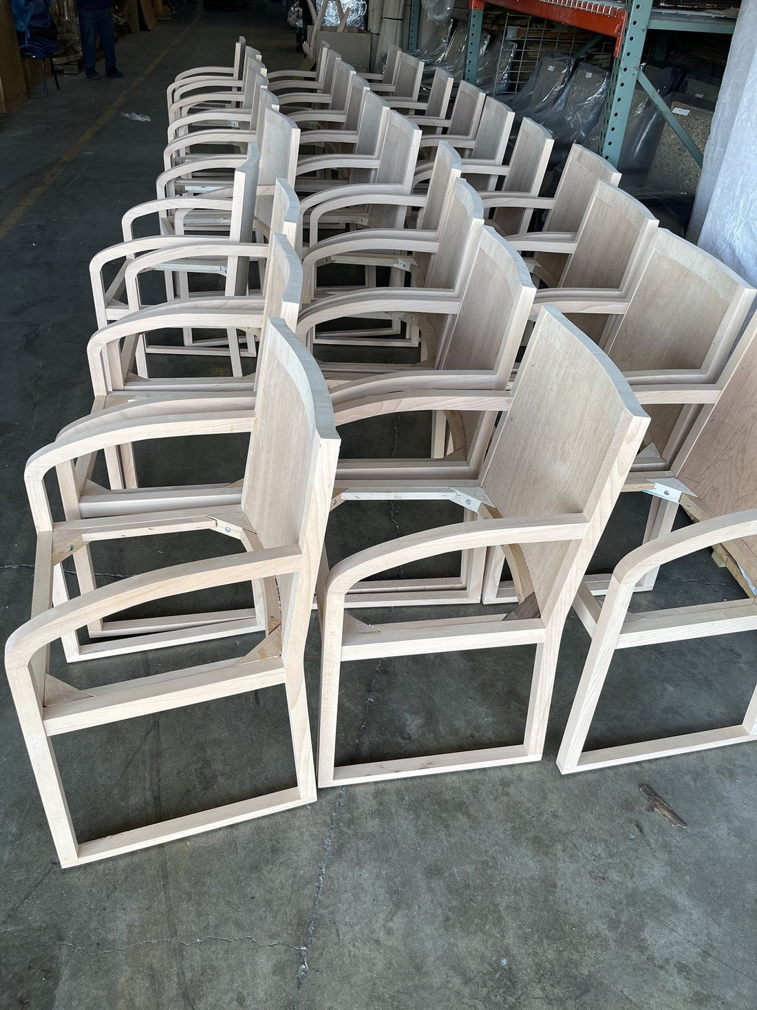 Rows of raw wood armchair frames with curved sled arms in the workshop