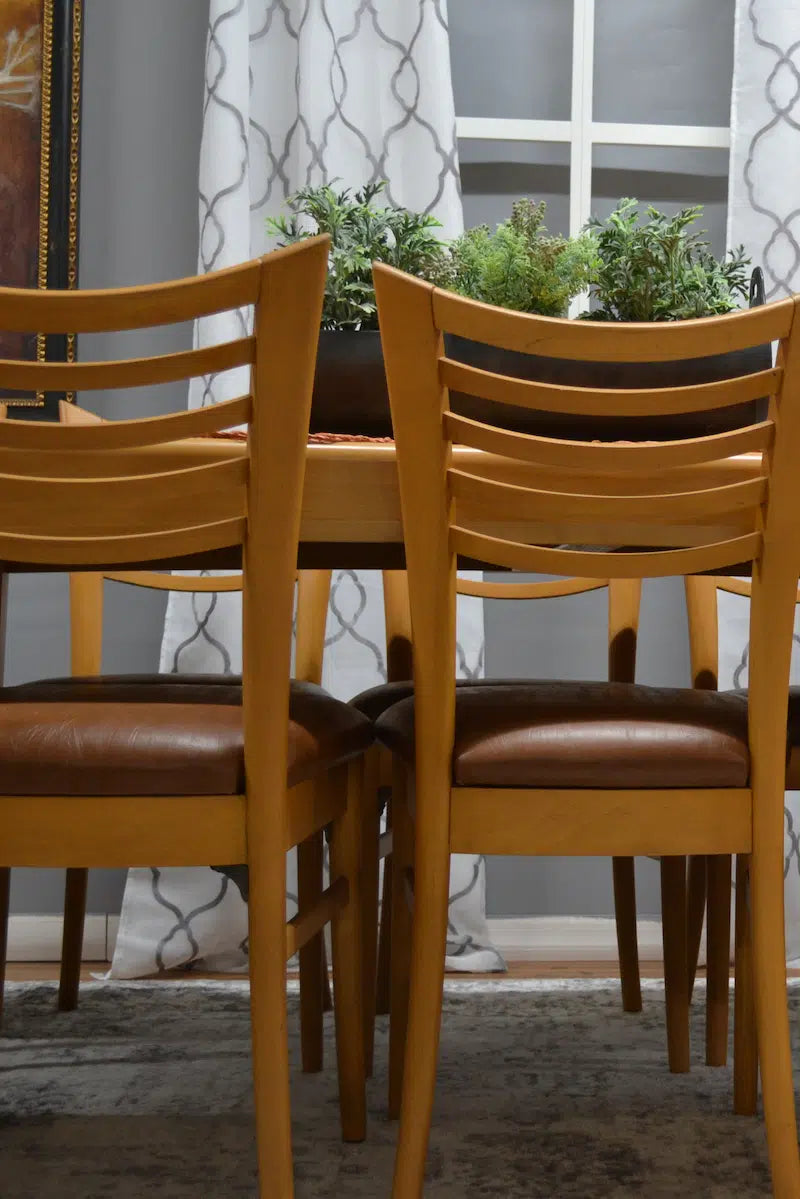 Two wooden chairs with brown leather seats in a room with a window and plants.