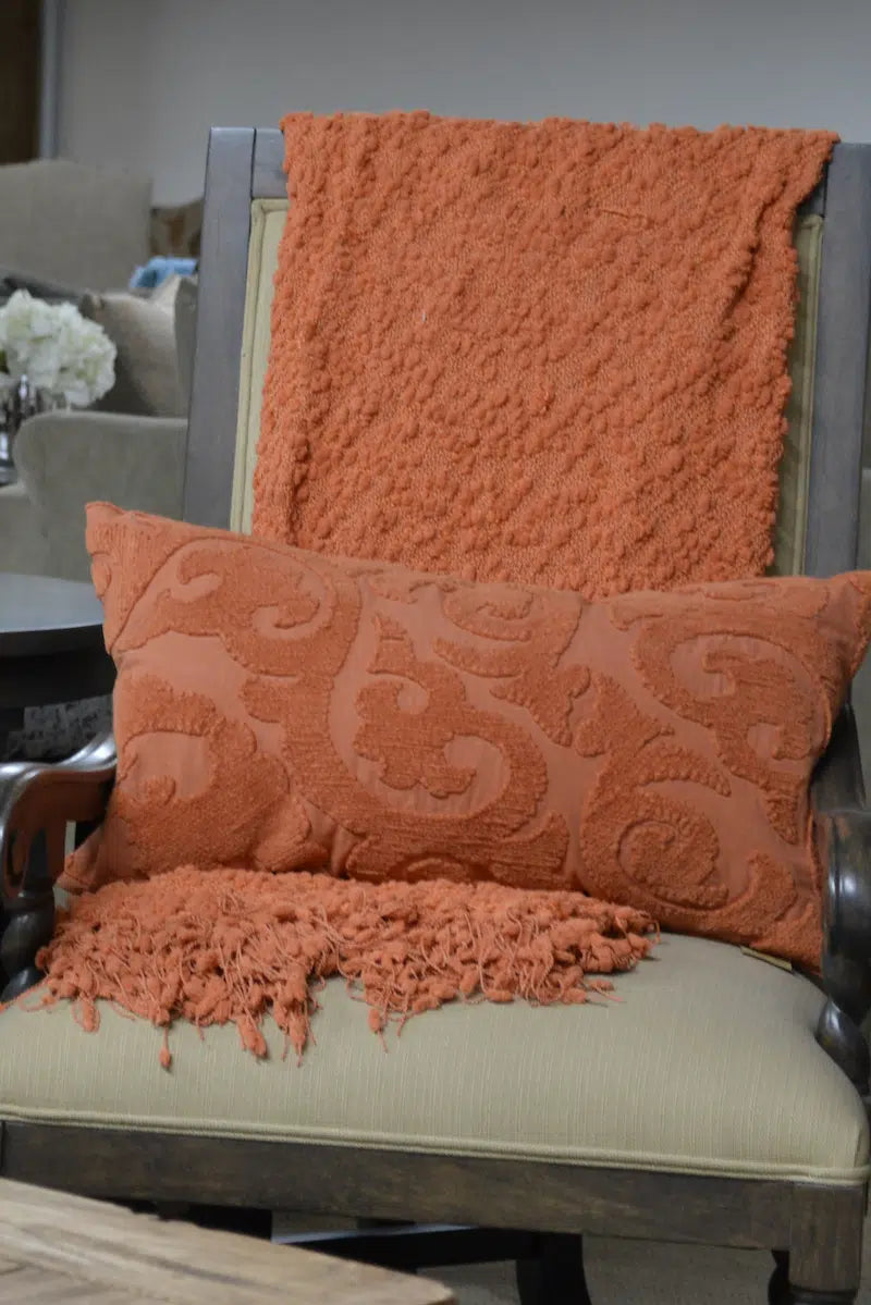 Chair with an orange textured throw blanket and pillow