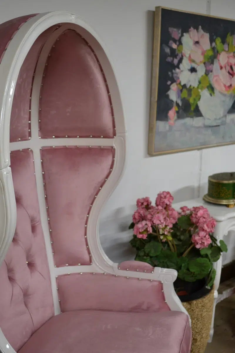 Pink balloon chair with white frame finish in a room with a floral painting and potted plant.