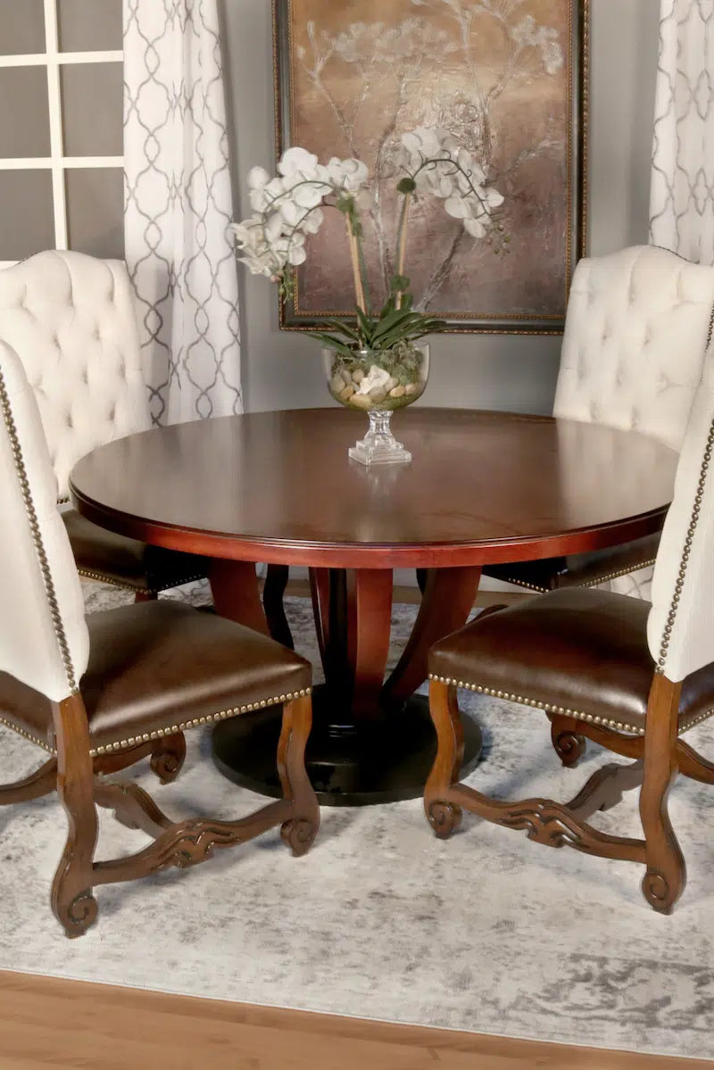 Round wooden dining table with four leather seat chairs in a room with decorative elements.